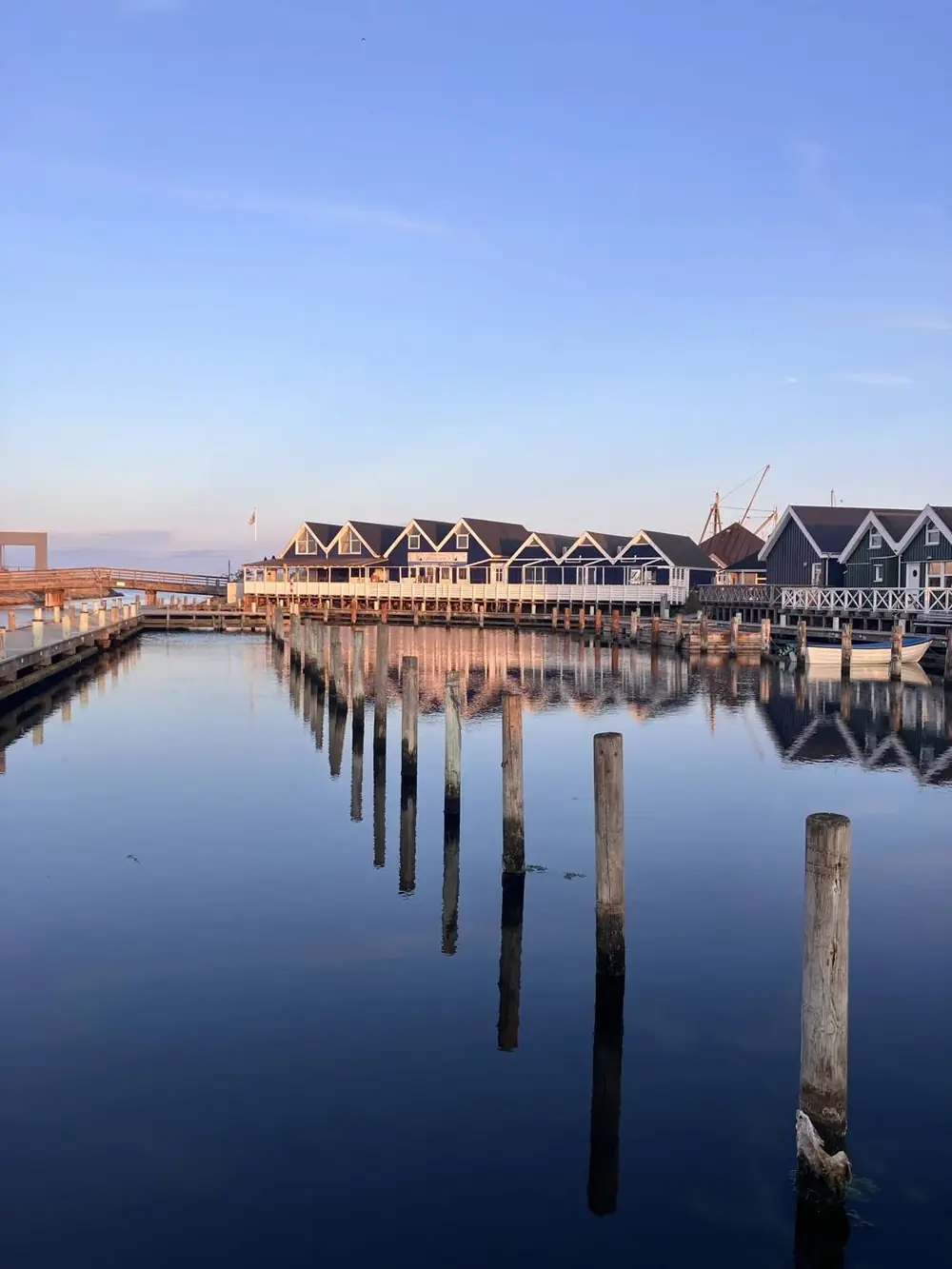 Sorte træhuse i Grenaa Marina spejler sig i vandet ved solnedgang